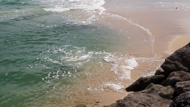 A beach with clear water, sandy shore, and large rocks.