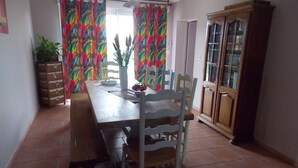 A dining area with a wooden table, white chairs, a cabinet, and colorful curtains.