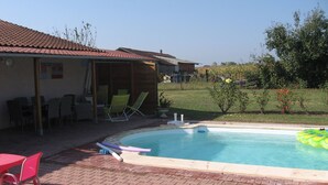 A swimming pool with a tiled deck, lounge chairs, and a small building with a covered patio.