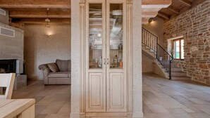 Un amplio salón con chimenea, un sofá, un aparador con puertas de vidrio y una escalera que lleva a un nivel superior con paredes de piedra.