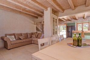 A cozy living room with a brown sectional sofa, a wooden dining table with chairs, and a kitchen area visible through an open doorway.