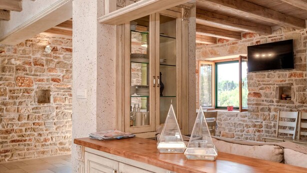 Una cocina rústica con paredes de piedra vista, vigas de madera y un mostrador de madera con objetos de vidrio decorativos.