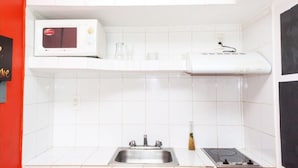Ett kök med vita kakelplattor, en mikrovågsugn, en brödrost och ett handfat.