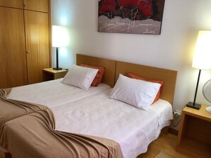 A double bed with white and orange bedding, a wooden headboard, and two bedside tables with lamps. - BARROS APARTMENT: Offers views of the ocean and mountains—visit Madeira’s many attractions. (Estreito De Câmara)