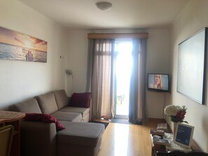 A living room with a sofa, a television, a window with curtains, and a painting on the wall. - BARROS APARTMENT: Offers views of the ocean and mountains—visit Madeira’s many attractions. (Estreito De Câmara)