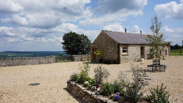 Une maison en pierre avec une allée en gravier et des parterres de fleurs.