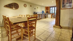 Un coin repas avec une table et des chaises en bois, une cuisine à l’arrière-plan et une grande poutre en bois au centre.
