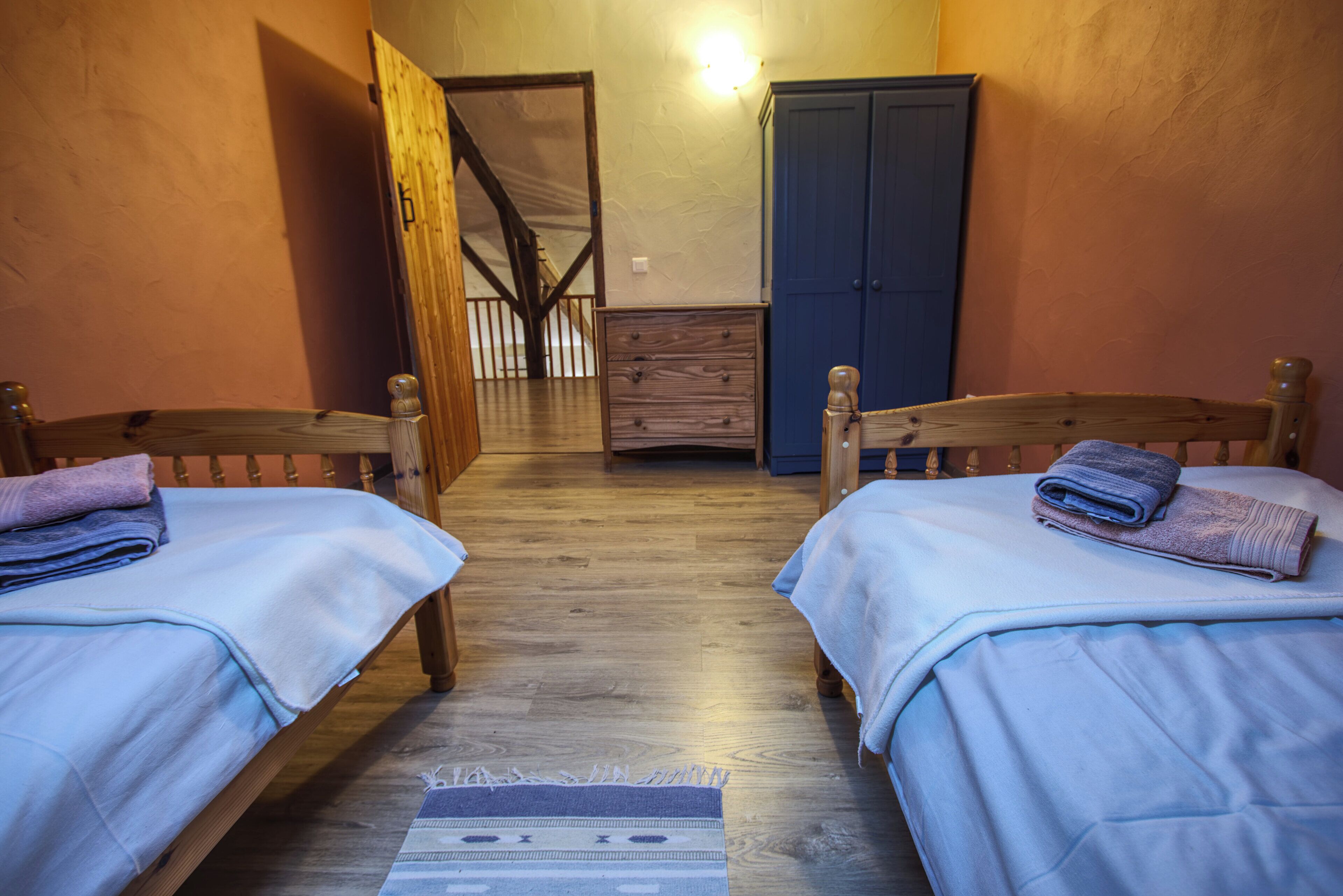 A room with two wooden beds, a wooden wardrobe, and a wooden chest of drawers.