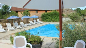 Une piscine entourée de verdure et d’un bâtiment en bois, avec des chaises longues et des parasols à proximité.
