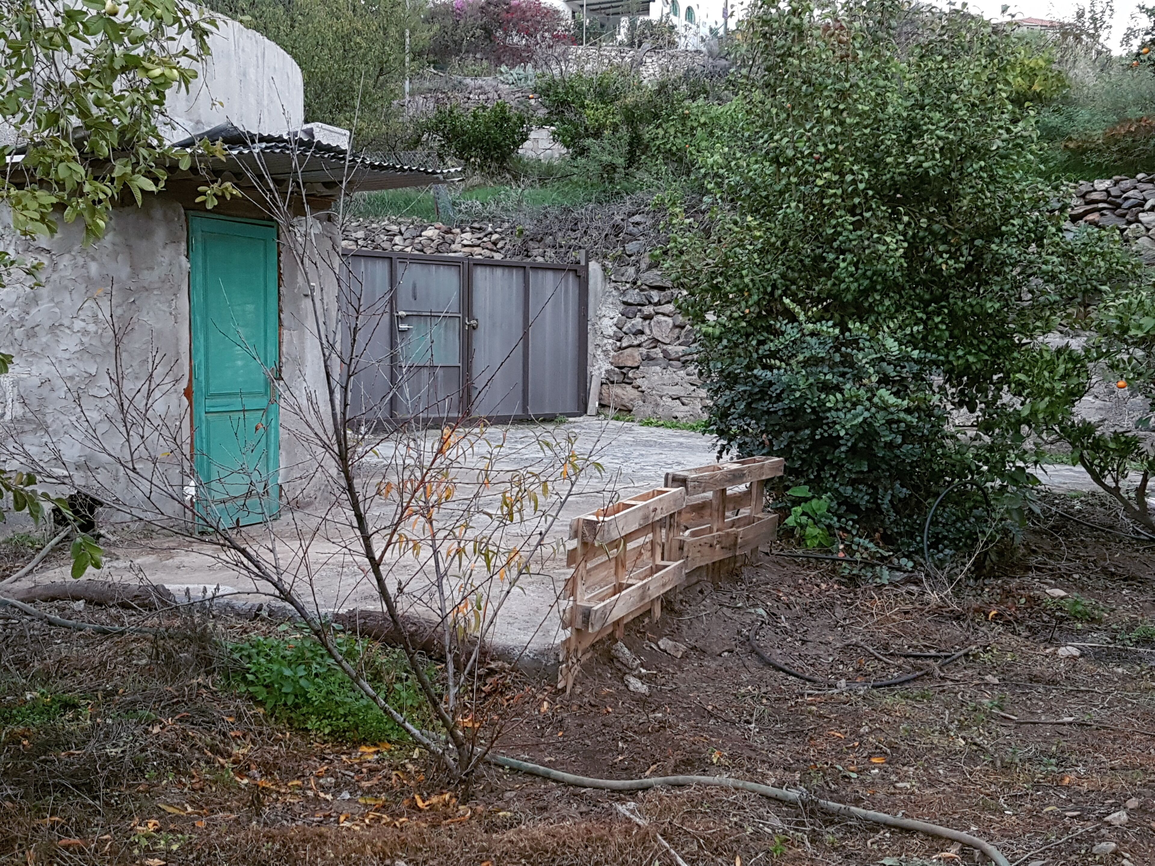 A rustic building with a green door, a stone wall, and a wooden staircase leading to a stone entrance.