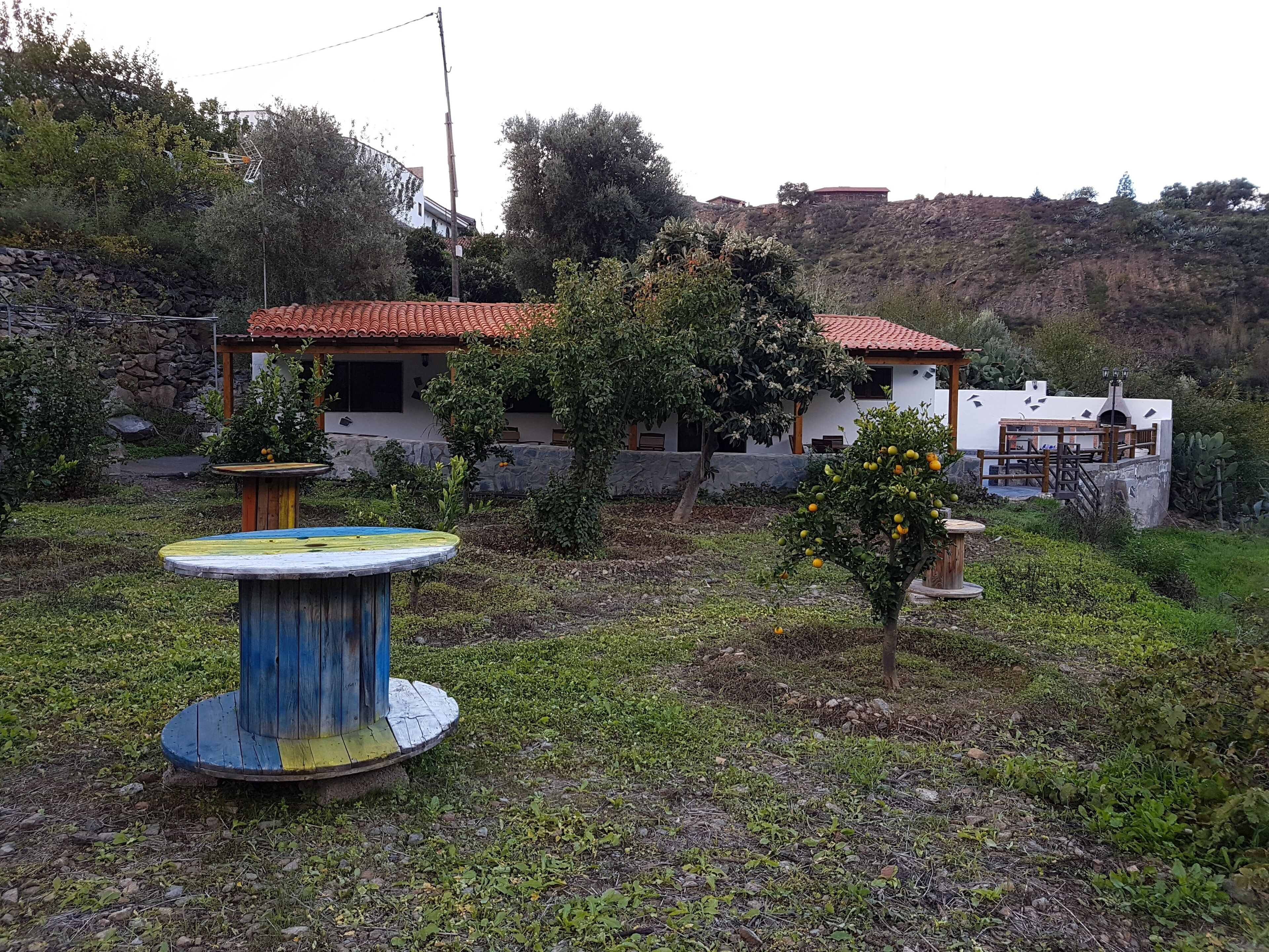A rustic house with a red-tiled roof, surrounded by greenery and a small garden with a round table.
