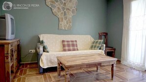A living room with a sofa, a wooden coffee table, a stone wall decoration, and a television on a wooden stand.