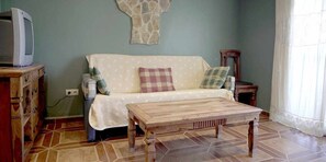 A living room with a sofa, a wooden coffee table, a stone wall decoration, and a television on a wooden stand.