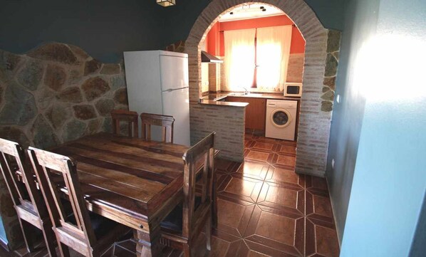 A compact kitchen with a stone wall, a white refrigerator, a washing machine, and a wooden dining table with chairs. - Self catering El Rincon de Piedra for 4 people (Enguídanos)
