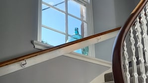 A staircase with a wooden handrail and white balusters, leading to a landing with a large window. - Bute House - Great Sea Views! (Rothesay)