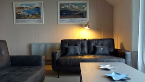 A living room with a dark leather sofa, a smaller armchair, and a coffee table with decorative items. Two framed posters are on the wall. - Bute House - Great Sea Views! (Rothesay)