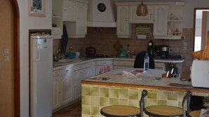 Eine Küche mit weißen Schränken, einem Kühlschrank, einer Kaffeemaschine und einem Spülbecken. Zwei Stühle stehen an der Arbeitsplatte.
