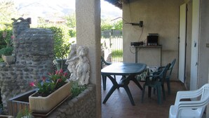 Eine Terrasse im Freien mit einer Steinmauer, einem Tisch, Stühlen und einem Grill.