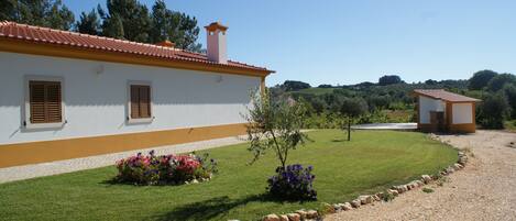 A white building with a red roof, a small garden with flowers, and a gravel driveway.