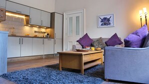 A modern kitchen with white cabinets and a wooden countertop. There is a dining area with a grey sofa and a coffee table. - Kirk View, 5 minutes from the station and local amenities. (Stirling)