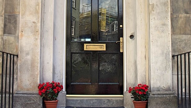 A black double door with a brass plate, flanked by two potted red flowers, and a stone building facade with a number '10' above the door. - Kirk View, 5 minutes from the station and local amenities. (Stirling)