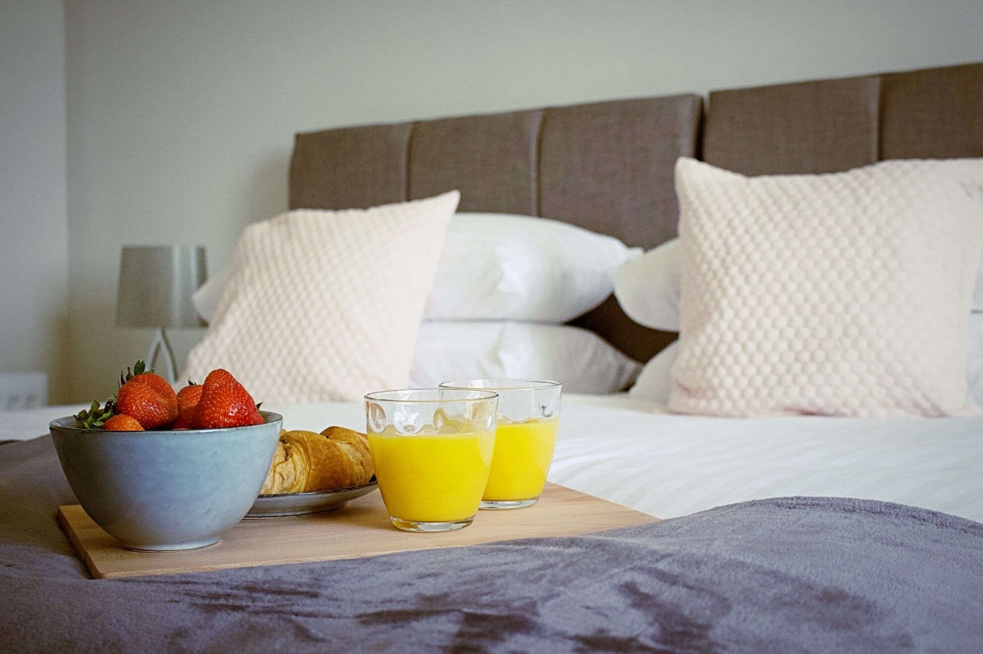 Morgenmad på sengen med jordbær, croissanter og glas med appelsinjuice.