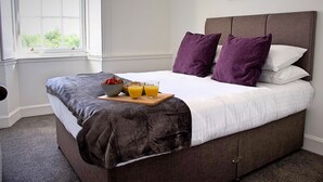 A neatly made bed with a gray headboard, white bedding, and purple pillows. A breakfast tray with fruit and orange juice is placed on the bed. - Kirk View, 5 minutes from the station and local amenities. (Stirling)