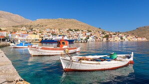 A harbor with boats docked, a hillside village in the background, and clear blue skies. - Halki Sea House, Luxury villa by the sea (HALKI ISLAND)