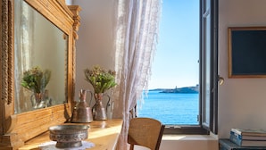 A room with a wooden table, a chair, a large mirror, a window with a view of the sea, and a vase with flowers. - Halki Sea House, Luxury villa by the sea (HALKI ISLAND)