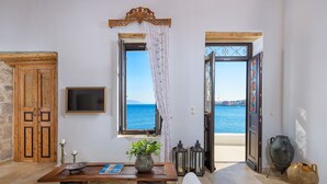 A room with a wooden table, a vase with flowers, a sofa, and a view of the sea through open doors. - Halki Sea House, Luxury villa by the sea (HALKI ISLAND)