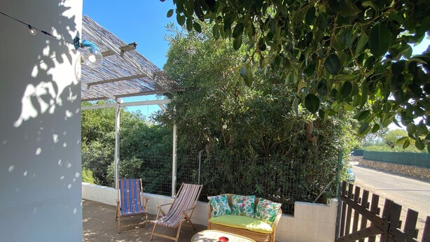 Un espace patio comprenant deux chaises longues à rayures, un canapé en osier et une petite table ronde.