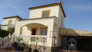 Una casa de dos pisos con balcón, mobiliario exterior y un aro de baloncesto.
