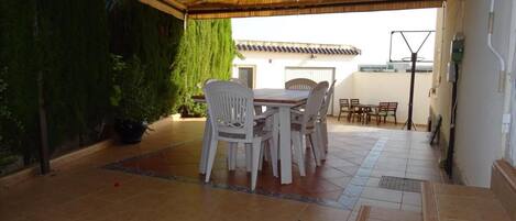 An outdoor patio with a covered seating area, a potted plant, and a tiled floor.