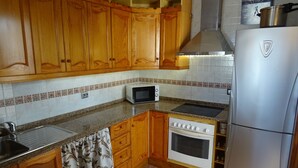 Una cocina con armarios de madera, microondas, horno y refrigerador.
