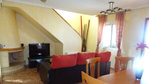 Una sala de estar con un sofá negro, cojines rojos, una mesa de comedor de madera y un televisor.