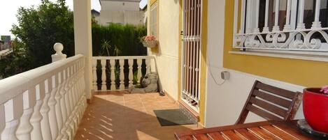 A balcony with a tiled floor, a wooden table, and a red bowl.