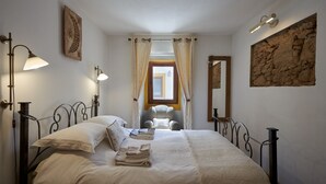 Un lit bien fait, avec une tête de lit, deux lampes de chevet, une chaise et un mur en pierre.