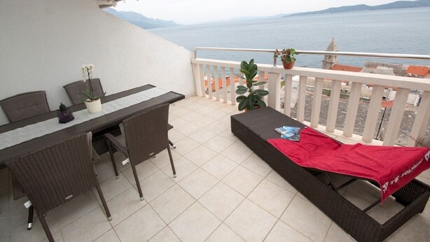 Ein Balkon mit Esstisch, Stühlen, einer roten Decke und Topfpflanzen.