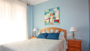 Ein Schlafzimmer mit einem Bett, zwei Nachttischen, einem Wandbild und einem Fenster mit Vorhängen.