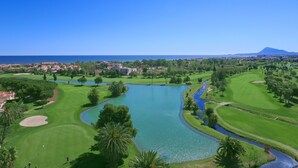 Ein Golfplatz mit einem großen Teich, umgebender Vegetation und einem Berg im Hintergrund.