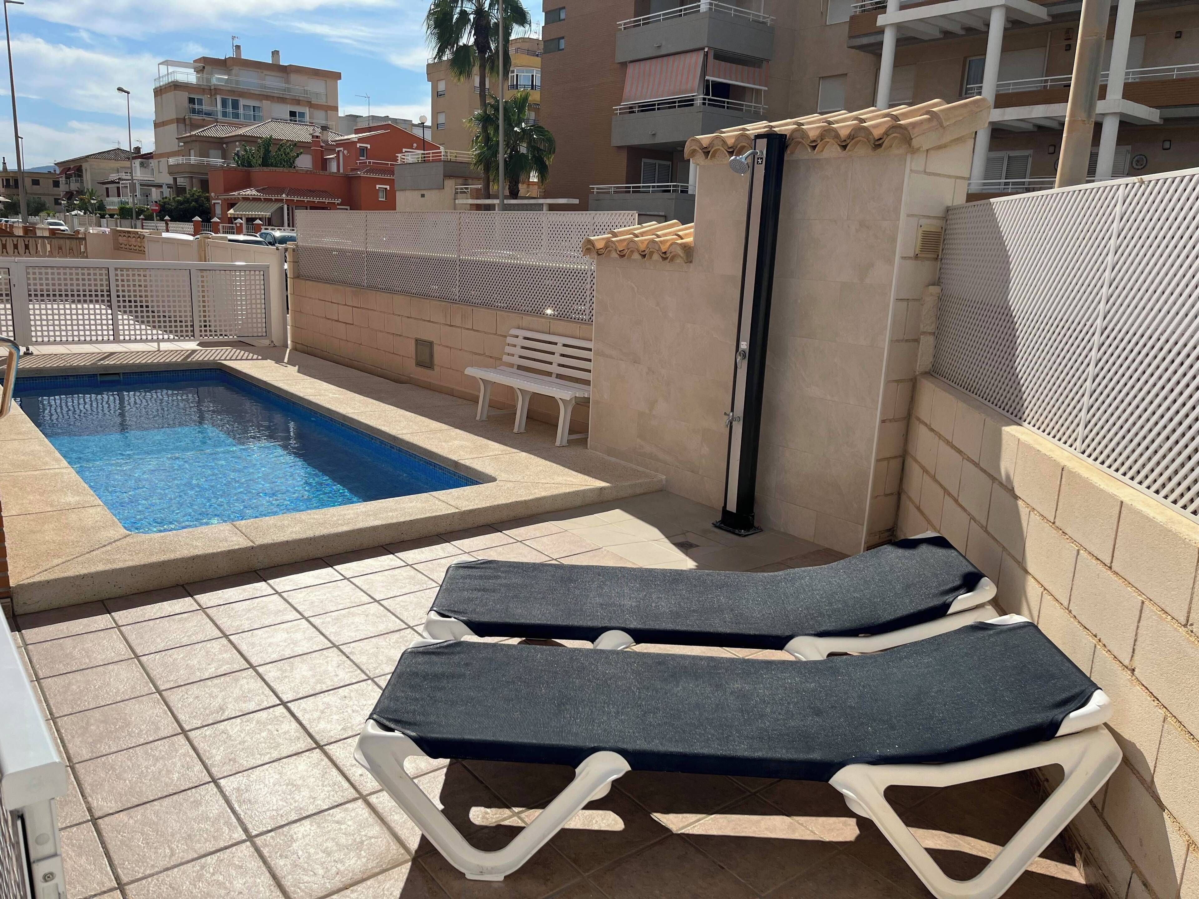 Una piscina con sillas de descanso, una banca y una reja.