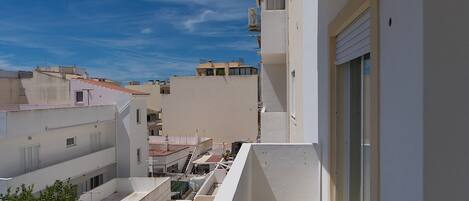 A residential building with a balcony, a window with a shutter, and a clear blue sky.