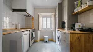 Cozinha moderna com armários brancos, bancada de madeira, forno embutido, máquina de lavar louça e máquina de lavar roupa, além de uma janela que proporciona luz natural.