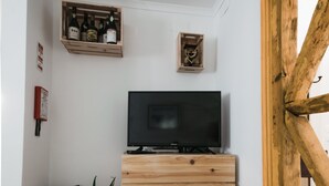 Quarto com um suporte de televisão de madeira, uma prateleira com garrafas, um vaso de planta e uma porta de madeira.