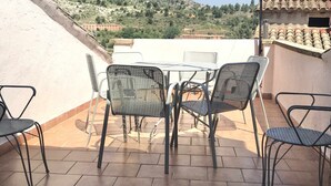 Pátio com mesa e cadeiras, com vista para uma paisagem montanhosa.