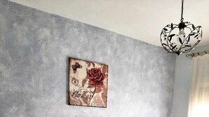Quarto com cabeceira de madeira, colcha branca, duas almofadas decorativas, mesa de cabeceira com abajur e um quadro na parede.