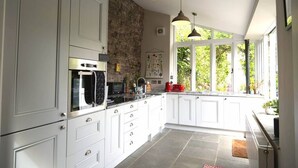 A modern kitchen with white cabinets, a stone accent wall, and pendant lighting. - Lovely property in the heart of Somerset (Wells)
