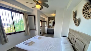 Une chambre d’hôtel avec un grand lit, un ventilateur de plafond, une vue sur l’extérieur par une fenêtre et un petit coin cuisine.