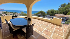 Une terrasse avec une table ronde et des chaises, un sol carrelé et une vue sur la mer et la verdure.