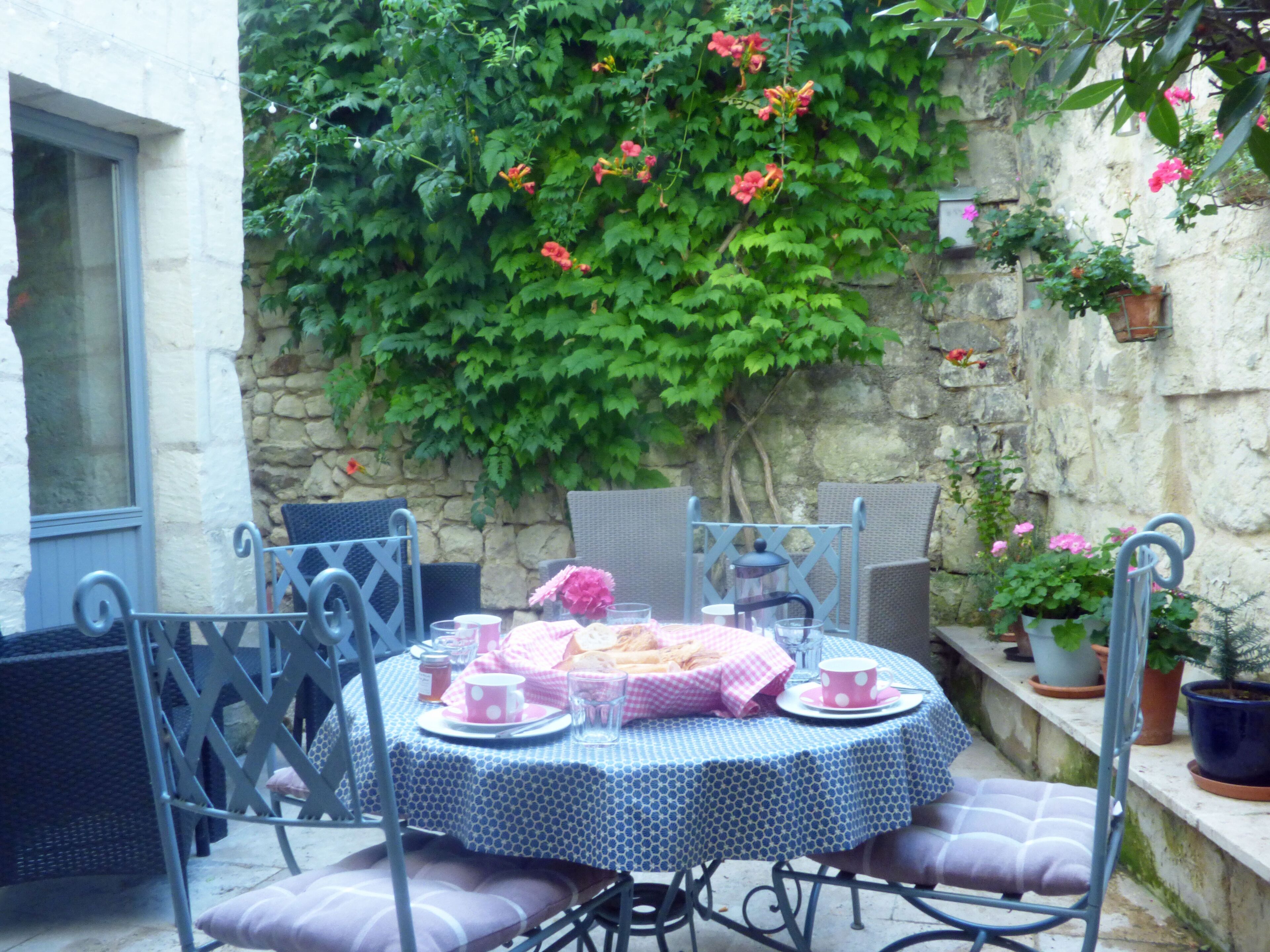 A round table with a checkered tablecloth, surrounded by wicker chairs with cushions.